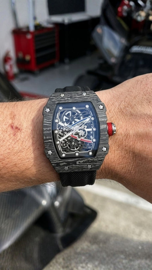 Close de relógio preto com mostrador vazado e detalhe vermelho na coroa, usado no pulso em uma garagem.