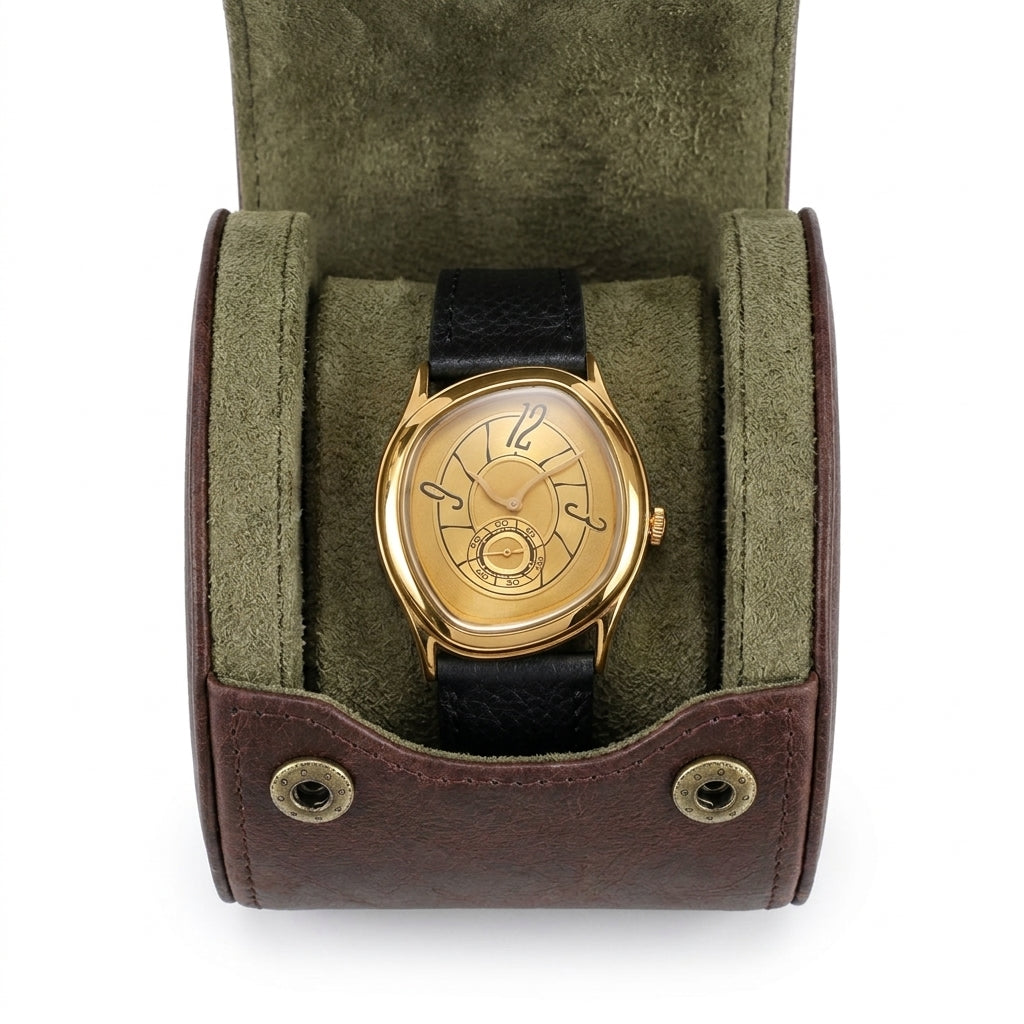 Semblantti dourado com pulseira preta sobre a almofada verde-oliva de um porta-relógio aberto de couro vinho, visto de cima.