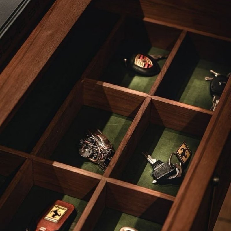 Gaveta de madeira luxuosa, exibindo chaveiros de carros de luxo, organizados sobre um fundo de veludo verde. Um detalhe de elegância e sofisticação no armazenamento de acessórios.